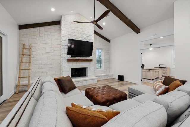 living room featuring ceiling fan, vaulted ceiling with beams, a fireplace, and light wood-type flooring