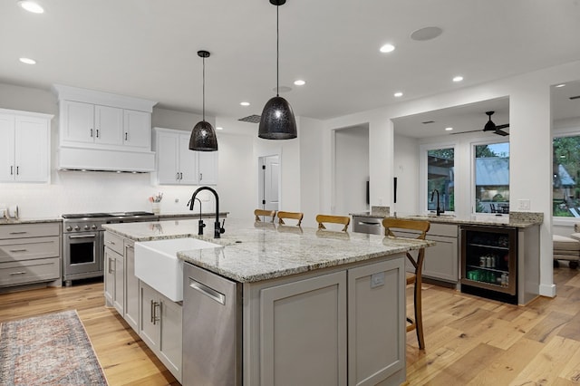 kitchen with a breakfast bar area, beverage cooler, light hardwood / wood-style flooring, stainless steel appliances, and a center island with sink