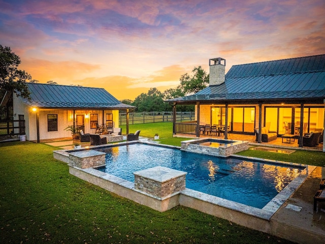 pool at dusk featuring a lawn, an in ground hot tub, and a patio