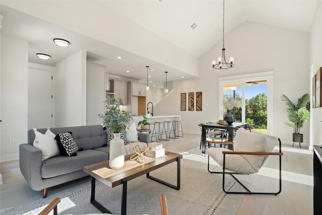 living room with an inviting chandelier, sink, high vaulted ceiling, and light hardwood / wood-style flooring