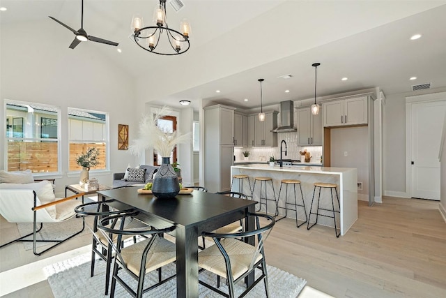 dining space featuring ceiling fan with notable chandelier, light wood-type flooring, sink, and high vaulted ceiling