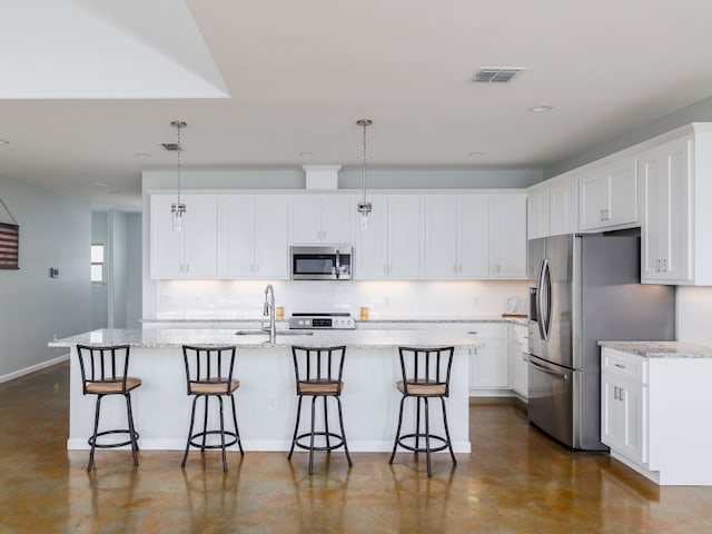 kitchen featuring white cabinets, a kitchen island with sink, appliances with stainless steel finishes, and hanging light fixtures