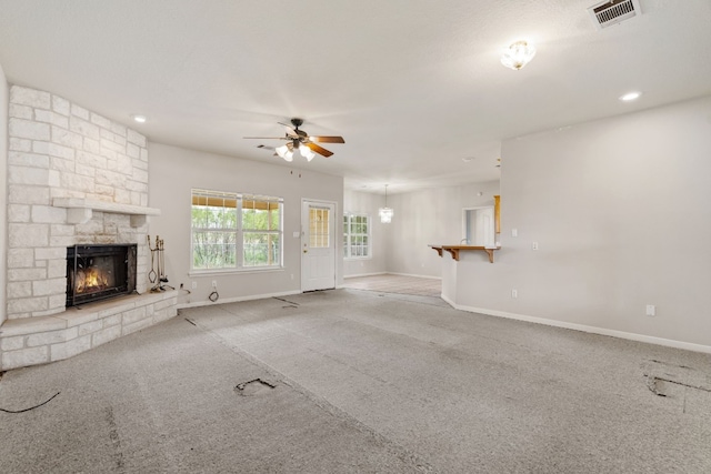 unfurnished living room featuring ceiling fan, a stone fireplace, and carpet floors