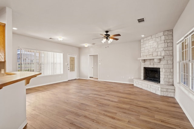 unfurnished living room with ceiling fan, a stone fireplace, and light hardwood / wood-style flooring