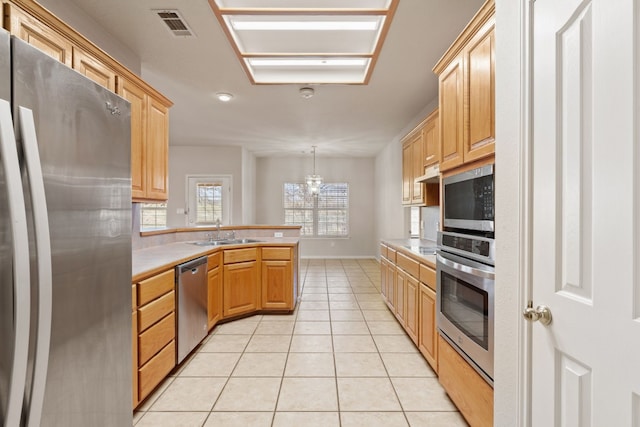 kitchen with sink, light tile patterned floors, appliances with stainless steel finishes, decorative light fixtures, and kitchen peninsula