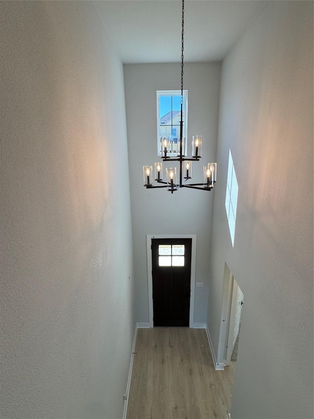 doorway to outside featuring light hardwood / wood-style floors, a towering ceiling, and a notable chandelier