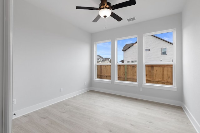 empty room with a ceiling fan, visible vents, light wood finished floors, and baseboards