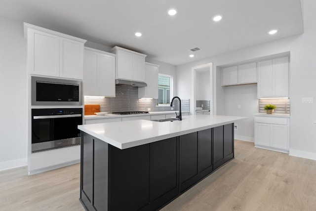 kitchen with oven, stainless steel microwave, a sink, and white cabinetry