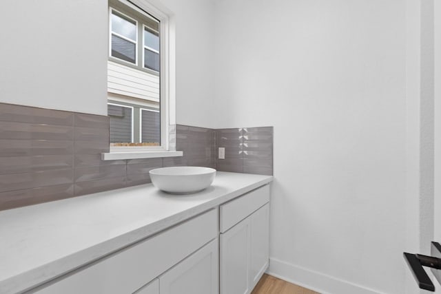 bathroom with baseboards, wood finished floors, vanity, and decorative backsplash