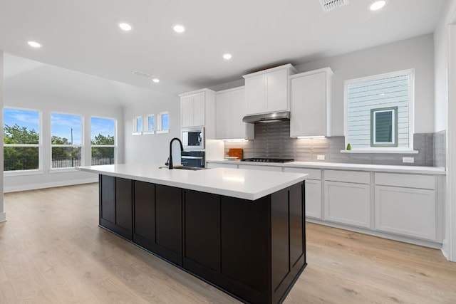 kitchen featuring light countertops, black cooktop, a sink, built in microwave, and under cabinet range hood