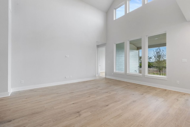 spare room with high vaulted ceiling, light wood-type flooring, and baseboards