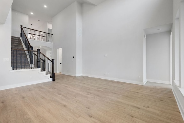 unfurnished living room featuring light wood finished floors, stairway, a high ceiling, and baseboards