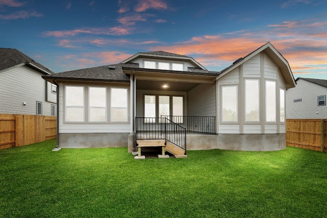 back of property at dusk with fence private yard and a lawn