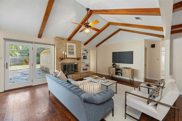 living room featuring ceiling fan, a brick fireplace, vaulted ceiling with beams, dark hardwood / wood-style flooring, and a textured ceiling