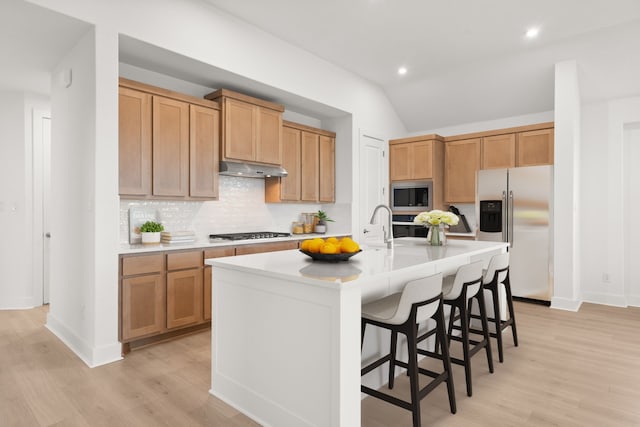 kitchen featuring vaulted ceiling, light wood-type flooring, stainless steel appliances, a center island with sink, and a breakfast bar area