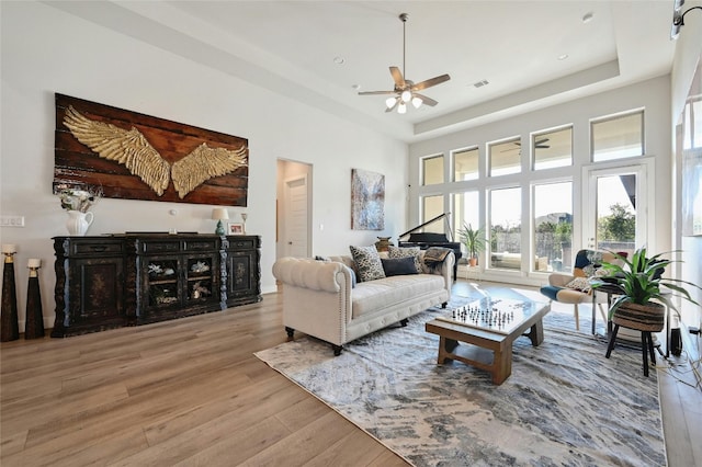 living room with wood-type flooring, a high ceiling, a tray ceiling, and ceiling fan