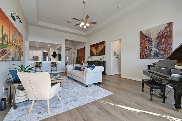 living room featuring light wood-type flooring, a tray ceiling, and ceiling fan