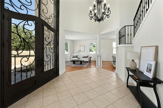 foyer with a towering ceiling, french doors, decorative columns, light hardwood / wood-style flooring, and an inviting chandelier