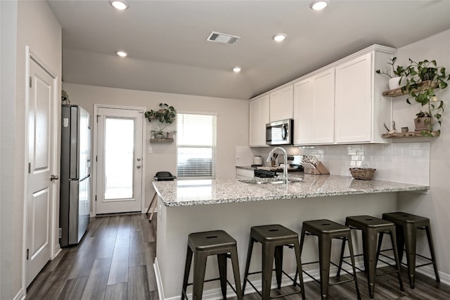 kitchen with a breakfast bar, dark wood-type flooring, white cabinets, appliances with stainless steel finishes, and light stone countertops