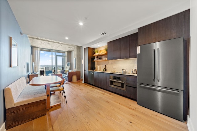 kitchen featuring dark brown cabinets, sink, light hardwood / wood-style flooring, stainless steel appliances, and decorative backsplash