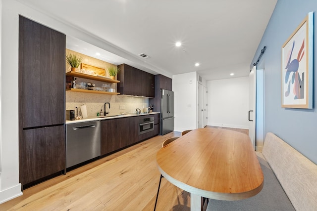 kitchen featuring sink, light hardwood / wood-style flooring, stainless steel appliances, decorative backsplash, and dark brown cabinetry