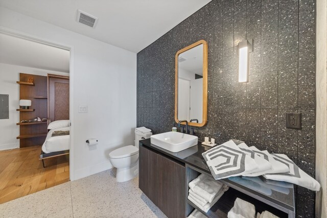 bathroom featuring tile walls, wood-type flooring, electric panel, vanity, and toilet