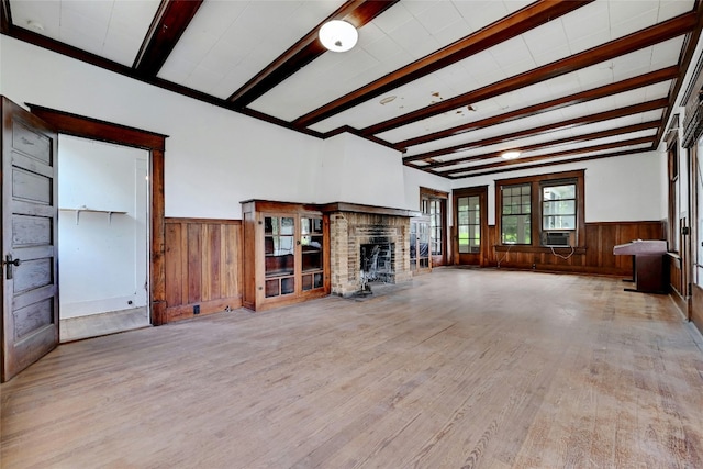 unfurnished living room with light hardwood / wood-style floors, wood walls, beamed ceiling, and a brick fireplace