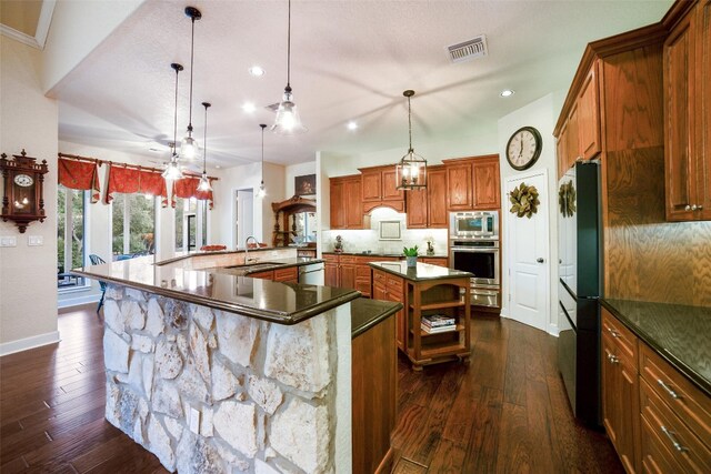 kitchen with appliances with stainless steel finishes, dark hardwood / wood-style flooring, pendant lighting, a large island, and sink