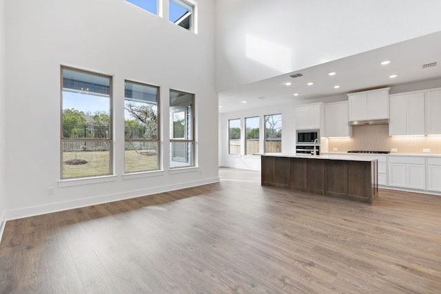 kitchen featuring light wood-style flooring, built in microwave, stovetop, white cabinetry, and backsplash