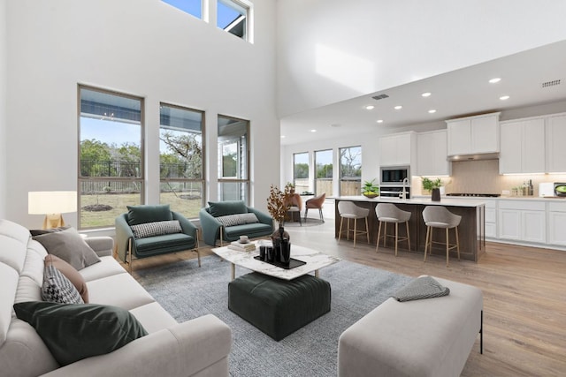 living room with visible vents, a towering ceiling, light wood-style flooring, and recessed lighting