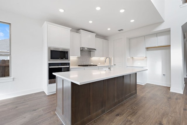 kitchen featuring tasteful backsplash, stainless steel microwave, a kitchen island with sink, stovetop, and black oven