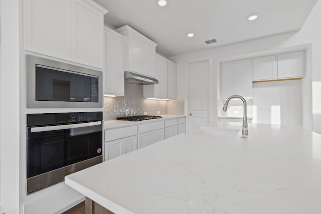 kitchen with built in microwave, under cabinet range hood, gas stovetop, stainless steel oven, and a sink