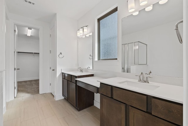 full bathroom with a stall shower, two vanities, a sink, and a spacious closet