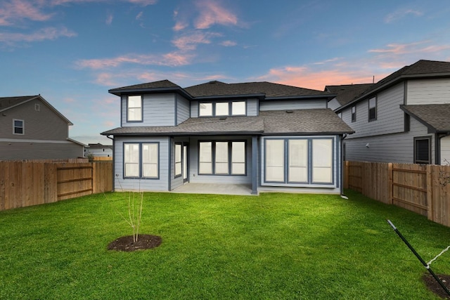 rear view of house with roof with shingles, a fenced backyard, a yard, and a patio