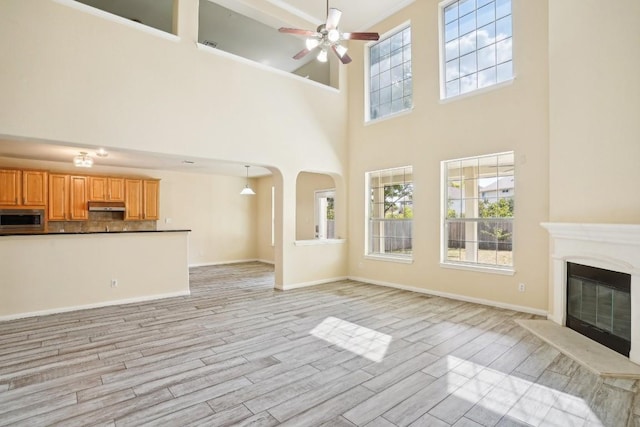 17006 Brewer Blackbird Dr, Pflugerville, TX 78660 - unfurnished living room with a high ceiling, ceiling fan, light wood-type flooring, a glass covered fireplace, and arched walkways