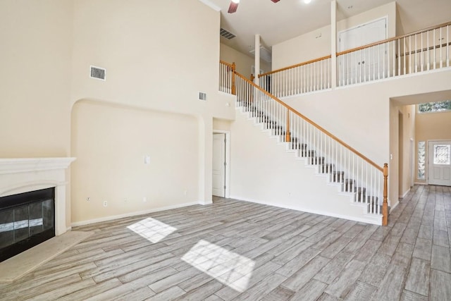 17006 Brewer Blackbird Dr, Pflugerville, TX 78660 - unfurnished living room with a high ceiling, wood finished floors, ceiling fan, stairway, and a glass covered fireplace