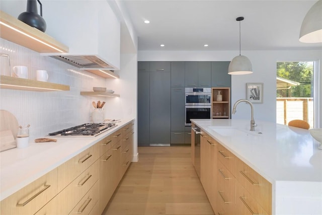 kitchen with sink, backsplash, hanging light fixtures, stainless steel appliances, and a center island with sink