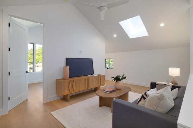 living room with lofted ceiling with skylight, ceiling fan, and light wood-type flooring