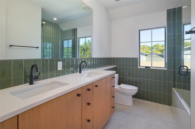 full bathroom featuring toilet, shower / bath combination with glass door, tile walls, vanity, and tile patterned flooring