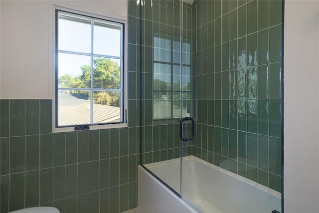 bathroom featuring tile walls, enclosed tub / shower combo, and toilet