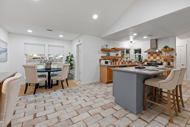 kitchen featuring a center island, wall chimney exhaust hood, backsplash, lofted ceiling, and stainless steel stove