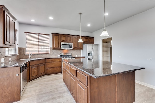 kitchen with appliances with stainless steel finishes, sink, light hardwood / wood-style floors, a kitchen island, and hanging light fixtures