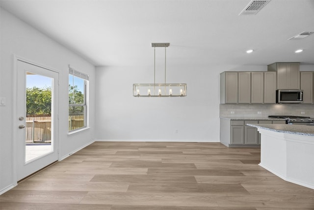 kitchen with gray cabinetry, backsplash, hanging light fixtures, appliances with stainless steel finishes, and light hardwood / wood-style floors