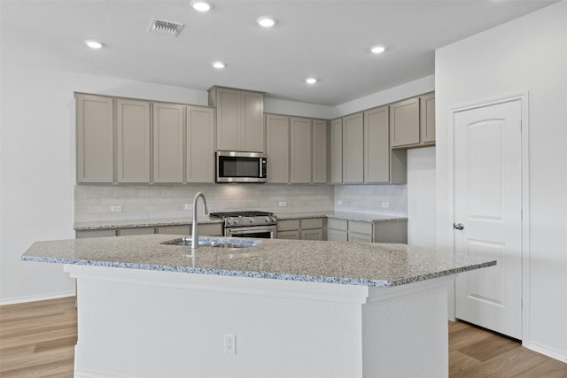 kitchen featuring a kitchen island with sink, stainless steel appliances, light stone counters, and light wood-type flooring