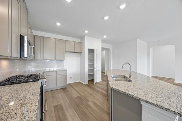 kitchen featuring sink, light stone countertops, an island with sink, appliances with stainless steel finishes, and light hardwood / wood-style floors