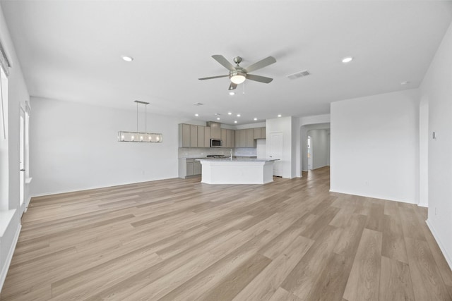 unfurnished living room with ceiling fan with notable chandelier, light hardwood / wood-style floors, and sink