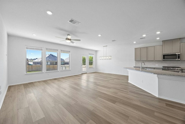 kitchen with light stone countertops, hanging light fixtures, stainless steel appliances, tasteful backsplash, and light wood-type flooring