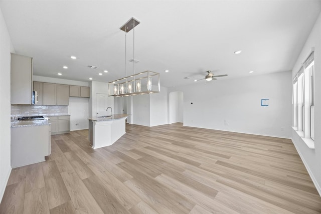 kitchen featuring decorative backsplash, a kitchen island with sink, pendant lighting, gray cabinets, and light hardwood / wood-style floors