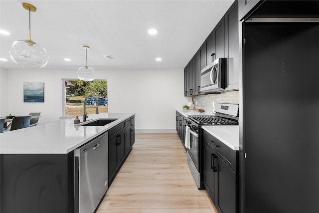 kitchen with hanging light fixtures, stainless steel appliances, light hardwood / wood-style flooring, a kitchen island with sink, and sink