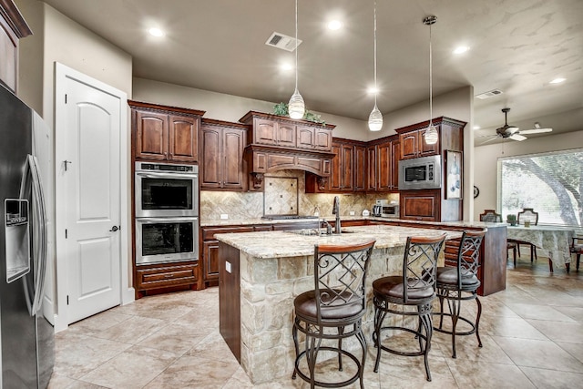 kitchen with ceiling fan, light stone counters, sink, a center island with sink, and appliances with stainless steel finishes